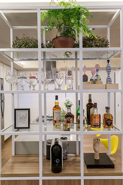 Гостиная зона имеет синюю акцентную стену, покрытую красочными элементами искусства. Двухместная серая кушетка украшена узорчатыми подушками с акцентом в мягких цветах и двумя шикарными фиолетовыми креслами добавляют дополнительные сидения и цвет в комнату. В углу на маленьком боковом столе находится милая лампа.