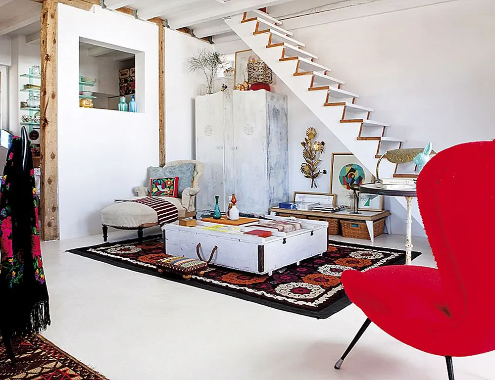 Частичная стена скрывает часть кухни. С другой стороны, уютный уголок для чтения, уголок для чтения украшен деревенским журнальным столиком и удобным креслом для отдыха. Лестница придает ей полу-частный вид.