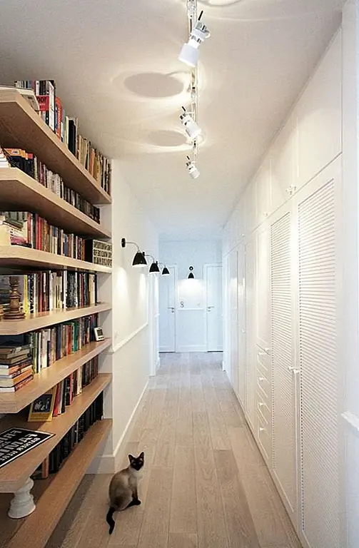 Поскольку небольшая квартира требует максимальной эффективности использования пространства, яркий, хорошо освещенный коридор включает в себя стену, полную шкафов, ящиков и шкафов - все окрашено в белый цвет, чтобы сохранить стилистическую простоту. Функциональный книжный шкаф с плавающими полками обеспечивает глубину и хранение.