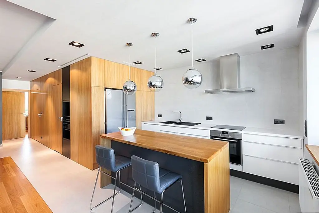 На кухонном острове есть деревянная раковина, которая координирует с остальными деревянными элементами в квартире, сохраняя сплоченный вид повсюду. Три металлических подвесных светильника, висящих над ним, создают прекрасную игру текстур, добавляя искру к этой области, а также к дизайну гостиной.