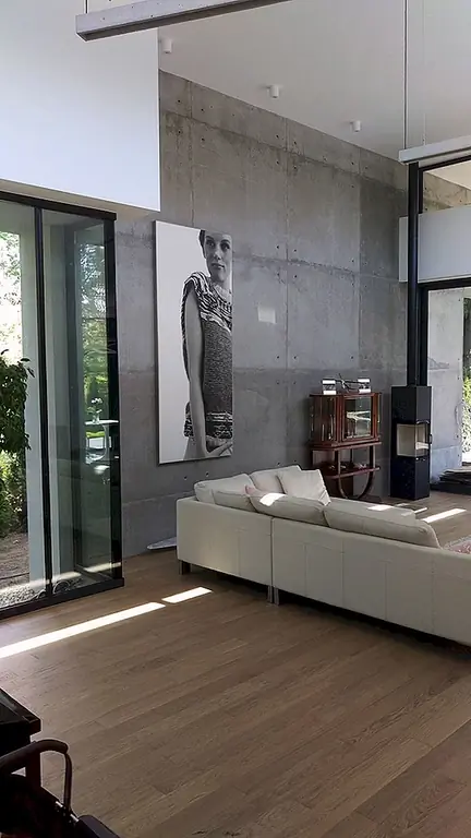 Дизайн интерьера прост. В гостиной незавершенная бетонная стена служит привлекательным фоном для камина и современного настенного искусства. Стена продолжается снаружи, обеспечивая бесшовное соединение между внутренними пространствами и наружным освещением. Диалог с внешним видом гладкий и красивый, несмотря на отсутствие застекленных фасадов или огромных отверстий. Поскольку сайт был шире к Западу, архитекторы превратили эту область в сад и позаботились разместить там террасу. На восток ворота, встроенные в забор, позволяют получить прямой доступ к гаражу с дороги.