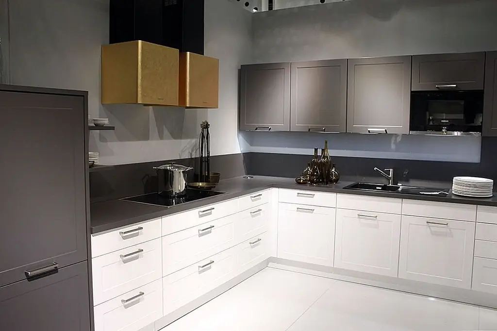 Взятие золота и белого цвета в качестве основных цветов, которые идут с серым в другом направлении, - это настоящая, свежая, современная кухня. Квадратные ручки Nobilia подчеркивают чистые линии пространства, а также стратегические горизонтальные блоки цвета. Конечно, изюминкой пространства является двустворчатый золотой капюшон над плитой, который так же очарователен, как и уникален.