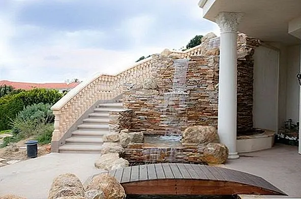 Эта потрясающая средиземноморская резиденция имеет красивую лестницу, которая выходит из каменной стены. Вода падает и падает в небольшой пруд. Это большое использование камня и камней.